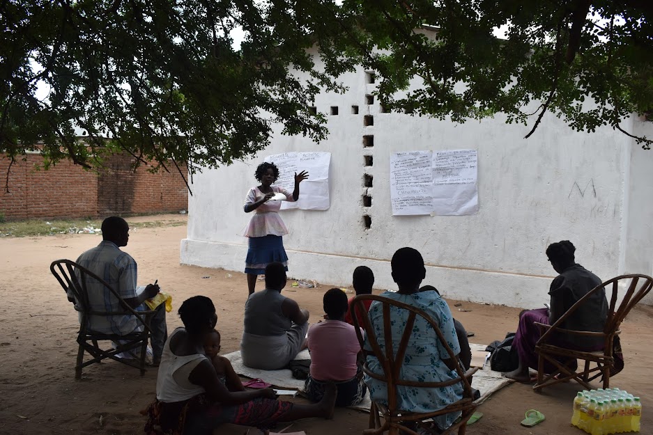 A woman teaching a group of people under a tree in Malawi